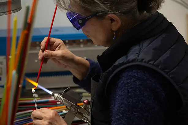 Une femme qui travaille le verre dans son atelier pour créer des bijoux