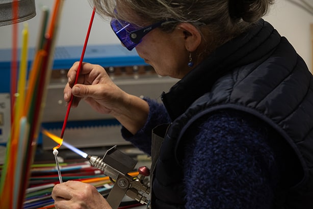 Une femme qui travaille le verre dans son atelier pour créer des bijoux